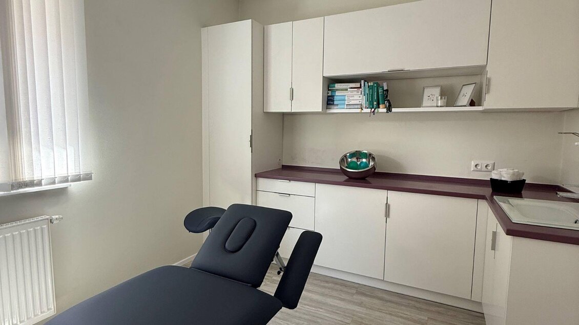 Ein moderner Behandlungsraum mit einem elektrischen Liegenstuhl und weißen Schränken. Das Licht ist hell und die Wände sind in neutralen Farben gestrichen. | © Lisa Schweitzer