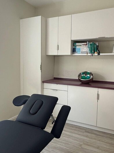 Ein moderner Behandlungsraum mit einem elektrischen Liegenstuhl und weißen Schränken. Das Licht ist hell und die Wände sind in neutralen Farben gestrichen. | © Lisa Schweitzer