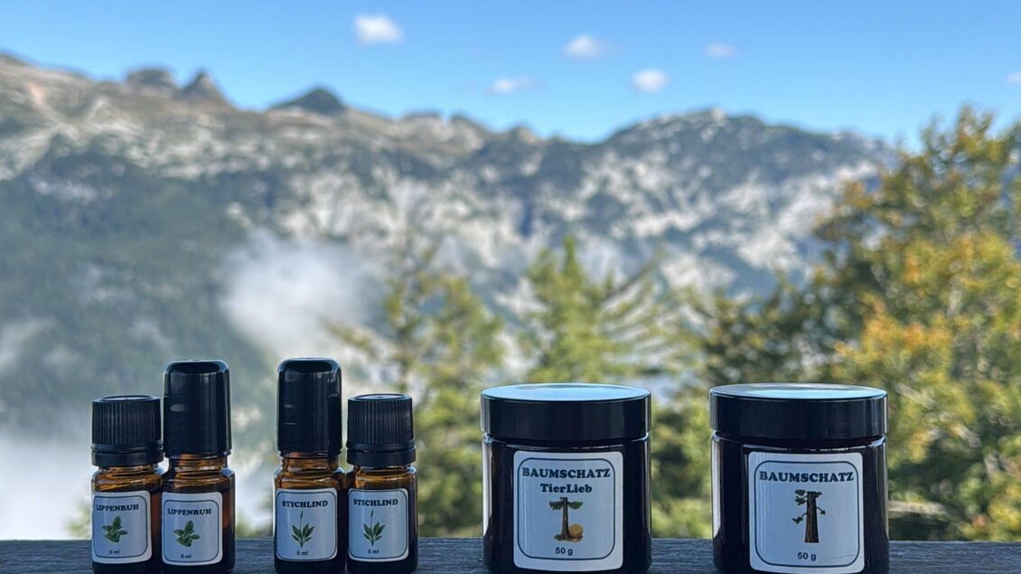 Eine Auswahl von ätherischen Ölen und Creme-Dosen steht auf einem Tisch mit einer beeindruckenden Berglandschaft im Hintergrund. Der Himmel ist klar, und die Natur umgibt die Produkte. | © Lisa Schweitzer