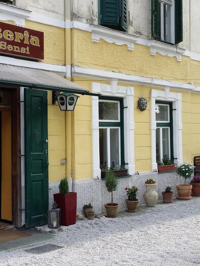 An inviting restaurant called "Osteria dei Sensi". The facade is yellow with many plants and flowers in pots. | © Osteria dei Sensi