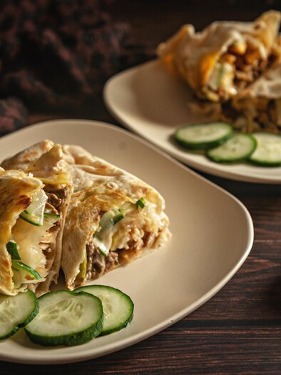 A plate with filled wraps, served with cucumber slices. In the background are garlic and onions. | © pexels-dee-dave