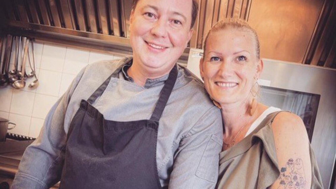 Mann in Kochkleidung und Frau lächelnd nebeneinander in einer Restaurantküche mit Edelstahlwand. | © PEP