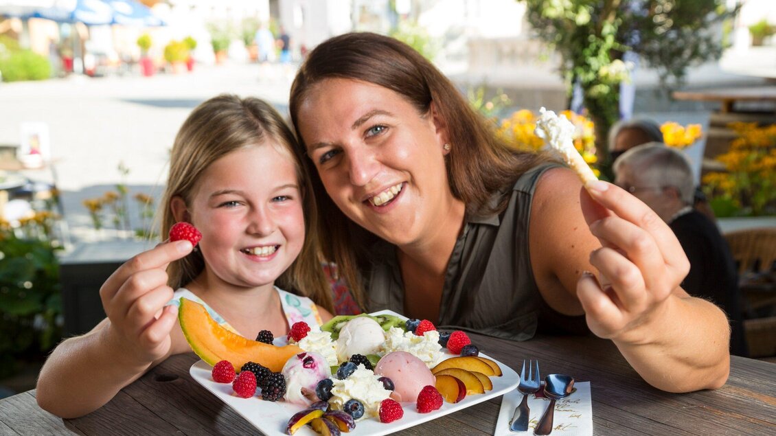 Eine Mutter und ihre Tochter genießen ein buntes Eisgericht mit frischen Früchten. Sie lächeln beide glücklich in die Kamera. | © TV Region Graz - René Vidalli