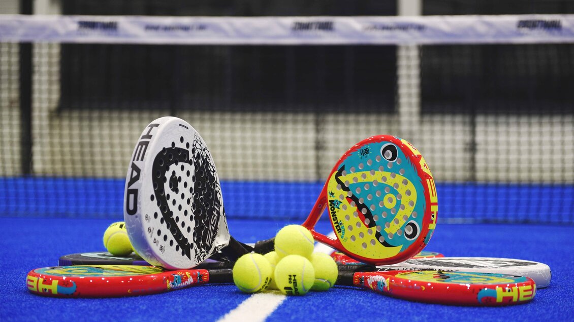 Mehrere bunte Padel-Schläger und gelbe Bälle liegen auf dem Indoor-Court in Kainbach bei Graz. | © Alexander Veit