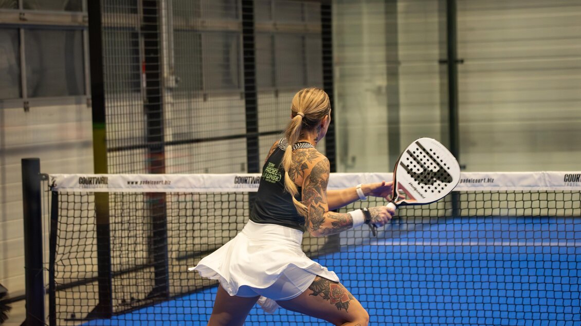 Tätowierte Frau im weißen Rock beim Padelspiel auf Indoor-Platz in Kainbach bei Graz. | © Alexander Veit
