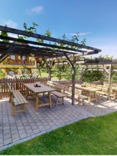 Eine gemütliche Terrasse mit Holzbank und Tisch unter einem Pergola-Baldachin. Im Hintergrund sind grüne Wiesen und ein klarer Himmel zu sehen. | © Helga & Robert | Panoramaschenke Kure