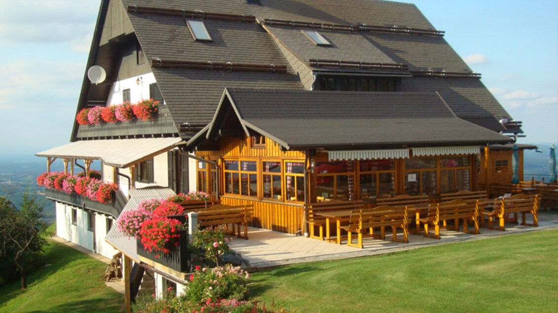 Ein hübsches Holzhaus mit einem großen Außenbereich und blühenden Blumen. Es bietet eine gemütliche Atmosphäre in einer naturnahen Umgebung. | © Panoramaschenke Tertinek | Fam. Tertinek