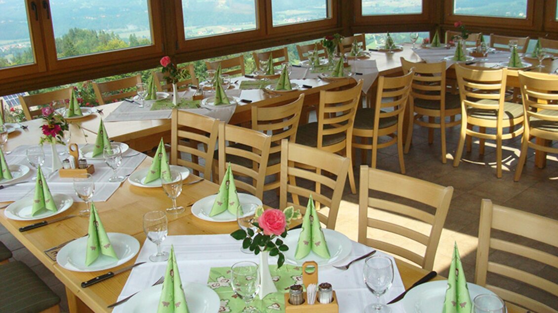 Ein schön dekorierter Restaurantbereich mit Tischen, die für Gäste vorbereitet sind. Große Fenster bieten einen Blick auf die umliegende Landschaft. | © Panoramaschenke Tertinek | Fam. Tertinek
