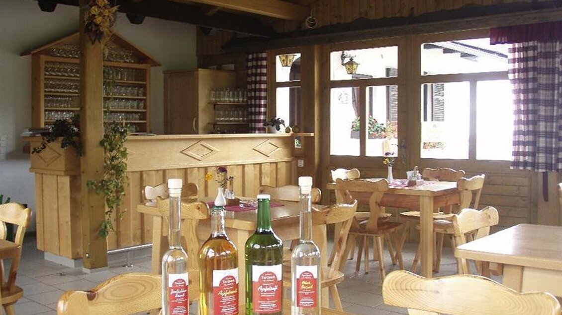 Ein gemütlicher Gastraum mit Holzmöbeln und einem gut beleuchteten Barbereich. Auf dem Tisch stehen verschiedene Flaschen Getränke. | © Panoramaschenke Tertinek | Fam. Tertinek