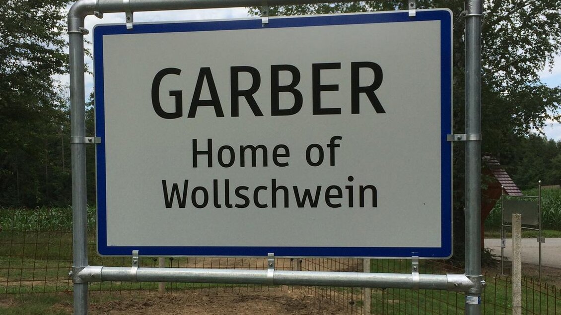 Ein Schild mit der Aufschrift „GARBER“ und „Home of Wollschwein“. Es zeigt den Eingang zu einem Bauernhof oder einer Region, die für Wollschweine bekannt ist. | © Panoramaturm - Wollschweinwanderung Garber
