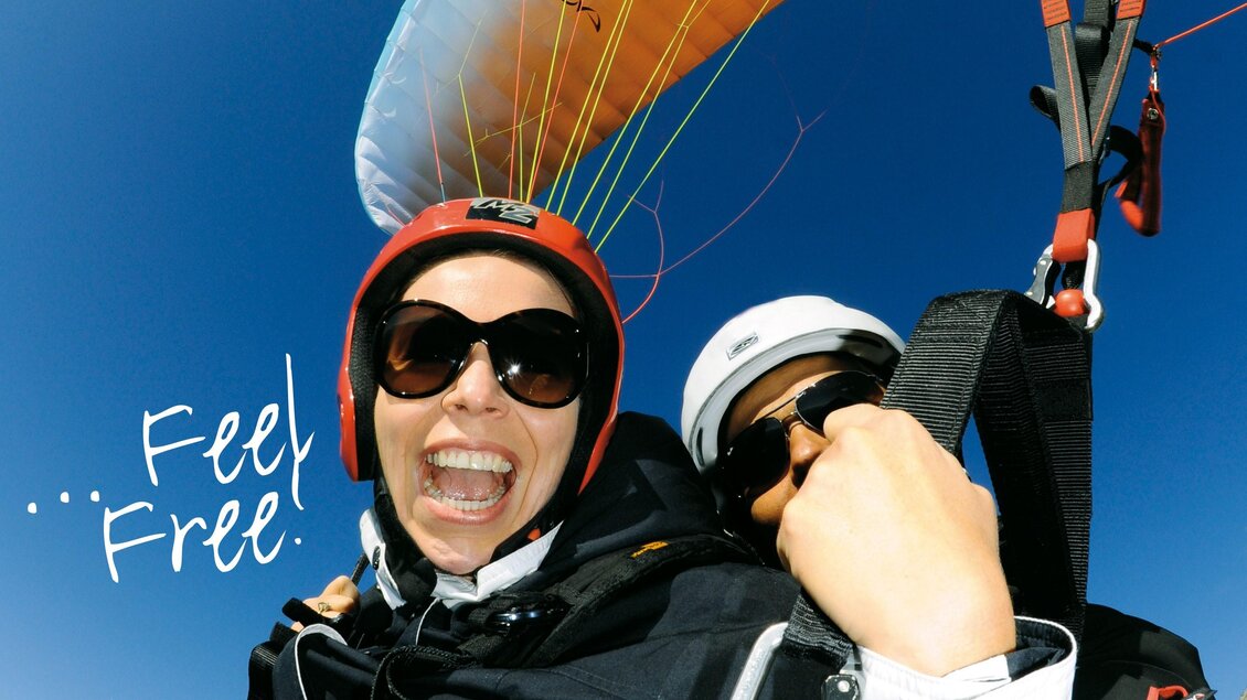 Ein glücklicher Passagier beim Paragliding, der in die Kamera lächelt. Im Hintergrund ist ein klarer blauer Himmel zu sehen. | © Firma Nova 