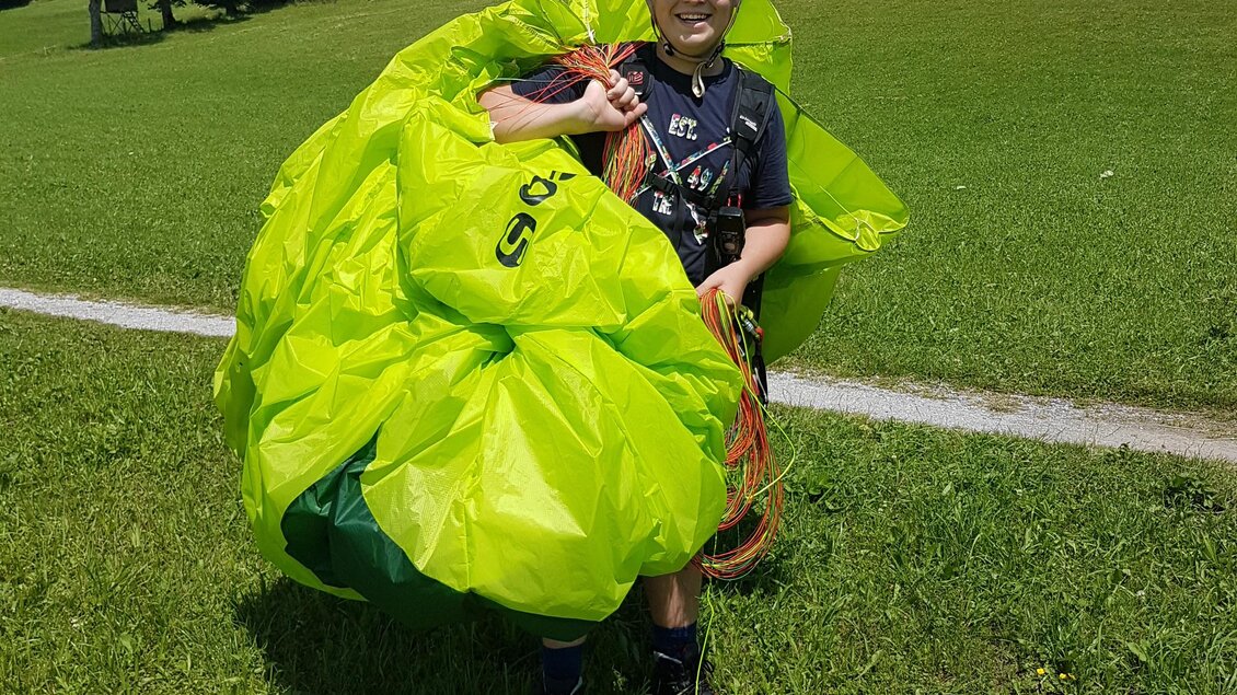 Eine Person steht auf einer Wiese und hält einen großen, leuchtend grünen Gleitschirm in den Händen. Sie trägt einen Helm und ist für das Gleitschirmfliegen bereit. | © Flugschule Aufwind 