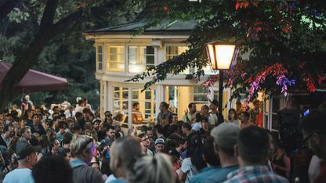 Eine belebte Veranstaltung im Freien mit einer großen Menschenmenge. Im Hintergrund ist ein charmantes Gebäude mit warmem Licht zu sehen. | © Parkhouse - Huber