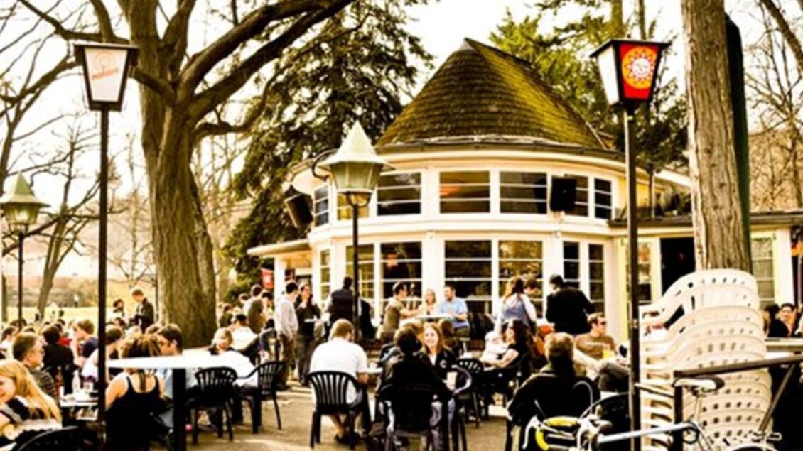 Ein belebtes Café im Freien mit vielen Gästen sitzt an Tischen. Umgeben von Bäumen und einer gemütlichen Atmosphäre. | © Parkhouse - Huber