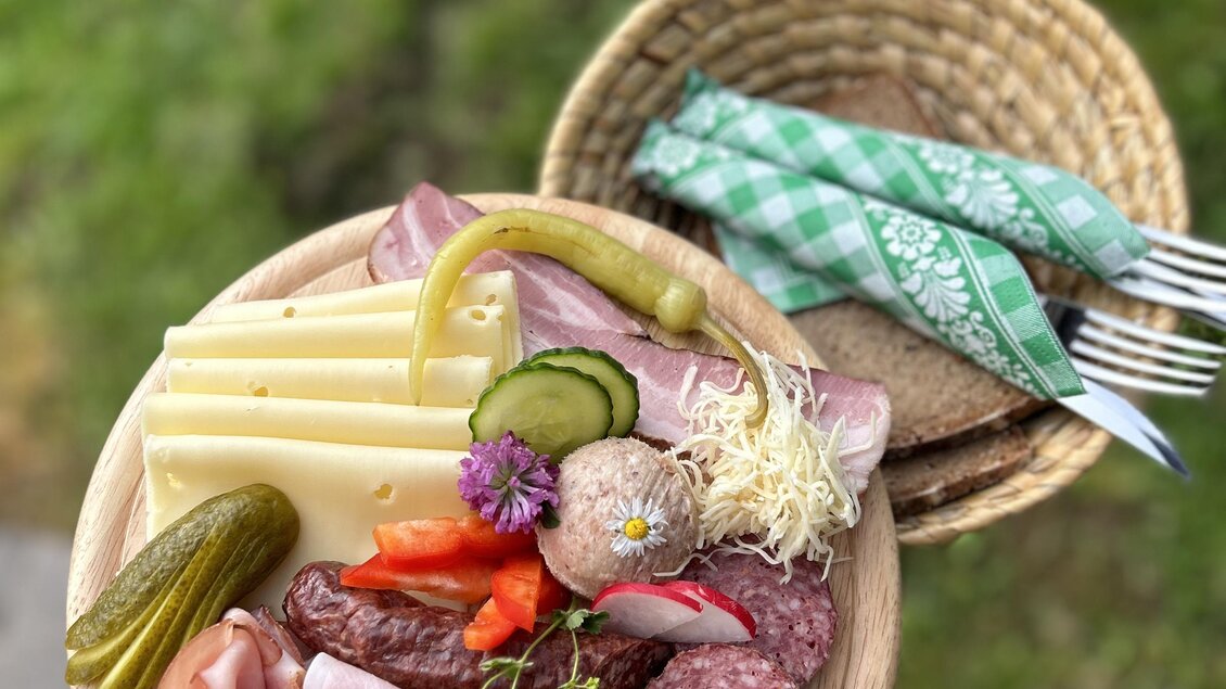 Ein schöner Holztablett mit verschiedenen Käsesorten, Wurst und eingelegtem Gemüse. Dazu gibt es ein Korb mit Besteck und Servietten. | © Theresa Perner 