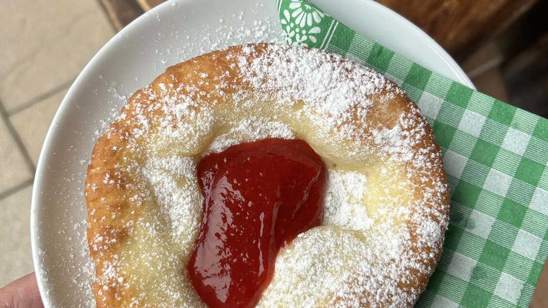 Ein frischer, gebackener Kuchen mit Puderzucker und einer roten Marmelade obenauf. Er liegt auf einem weißen Teller mit einem grünen Serviettenstück. | © Theresa Perner