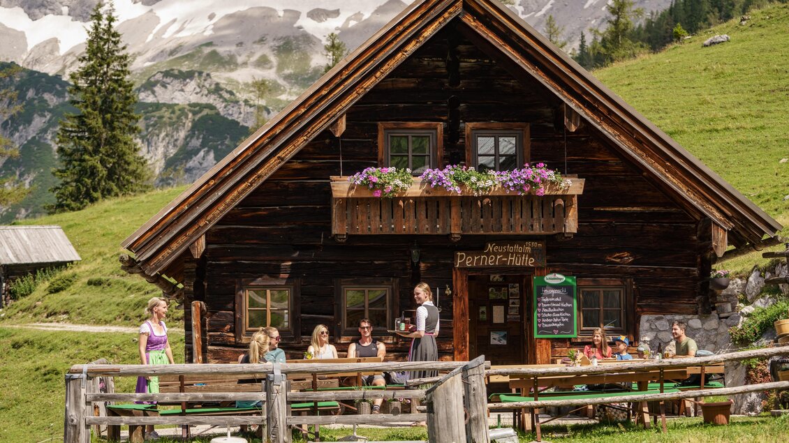 Eine gemütliche Berghütte mit blühenden Blumen auf dem Balkon. Besucher genießen die Aussicht in der malerischen Alpenlandschaft. | © TVB Schladming-Dachstein/Christine Höflehner
