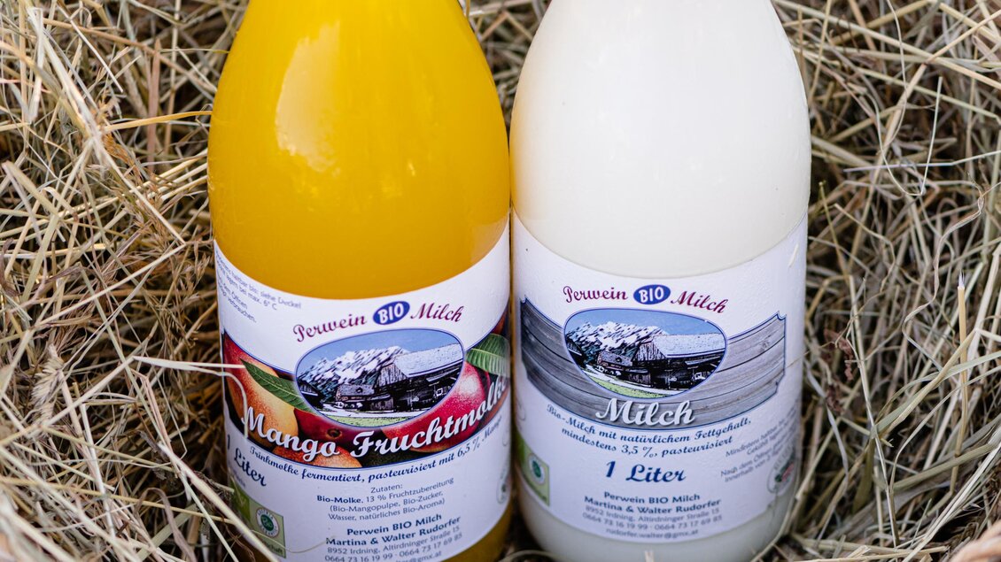 Zwei Flaschen Getränk stehen auf Heu. Links ist eine Flasche mit Mango-Saft und rechts eine Flasche Milch. | © Martina Siebenhandl