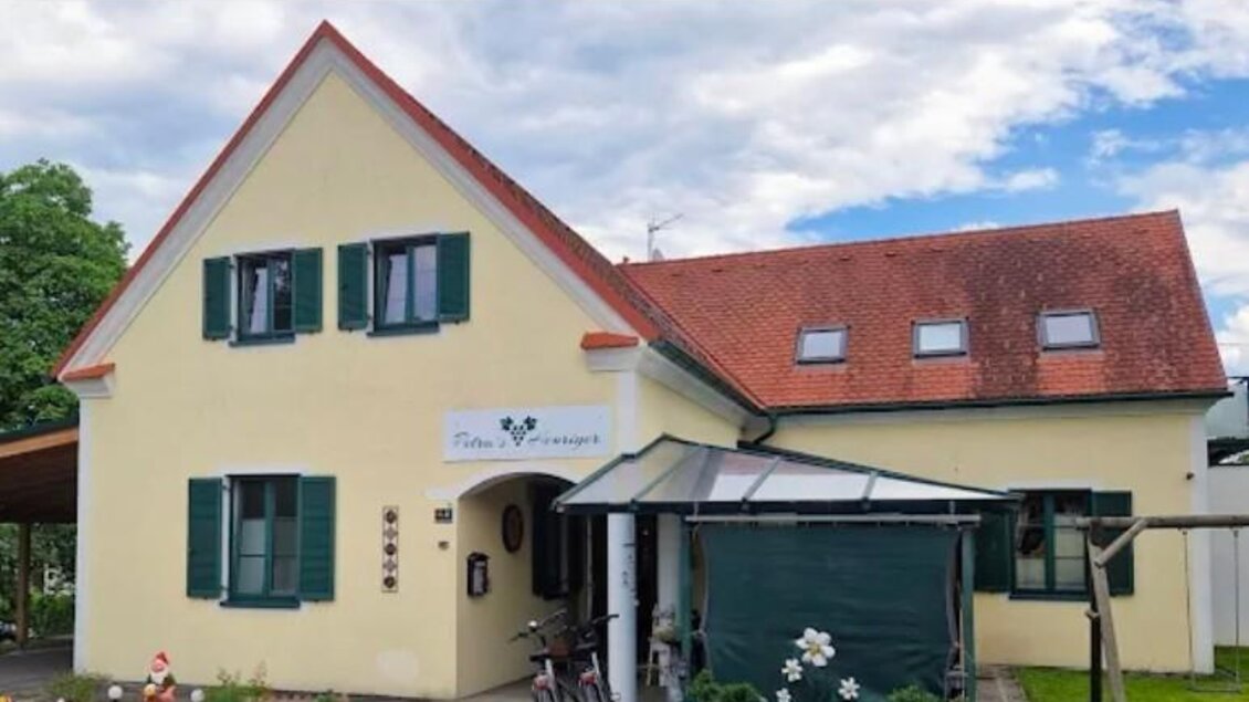 Ein gelbes Haus mit grünem Fensterladen und rotem Dach. Es gibt ein Fahrrad vor der Tür und einen kleinen Garten. | © Janisch