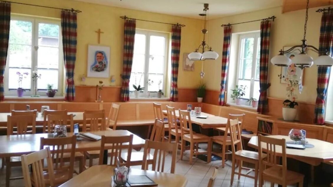 Ein gemütlicher Speisesaal mit Holztischen und -stühlen. Die Wände sind hell gestrichen und mit Fenstern und Vorhängen dekoriert. | © Janisch