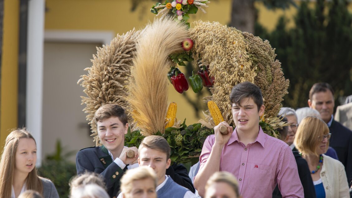 Eine Gruppe von Menschen feiert mit einer kunstvoll dekorierten Erntekrone. Die Stimmung ist festlich und gesellig. | © Kurkommission Bad Blumau