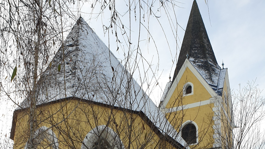 Eine gelbe Kirche mit markanten, spitzen Türmen. Der Schnee auf den Dächern und die winterlichen Äste verleihen der Szene eine ruhige Atmosphäre. | © Daniela Casari