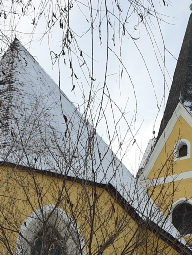 Eine gelbe Kirche mit markanten, spitzen Türmen. Der Schnee auf den Dächern und die winterlichen Äste verleihen der Szene eine ruhige Atmosphäre. | © Daniela Casari