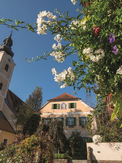 Ein malerisches Dorf mit einer schönen Kirche und bunten Blumen im Vordergrund. Der Himmel ist klar und blau. | © Sonja Hofinger
