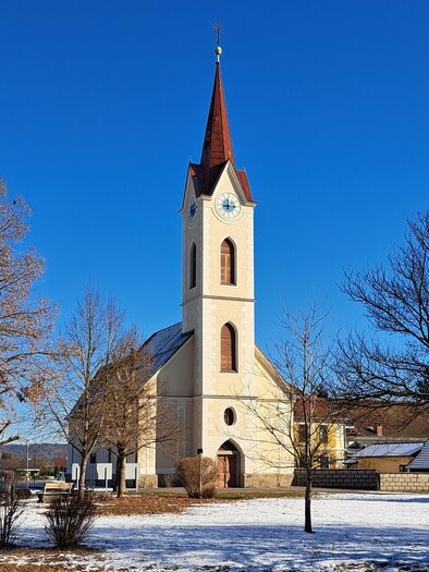 Eine Kirche mit einem spitzen Turm steht in einer schneebedeckten Landschaft. Der Himmel ist klar und blau. | © P. Gustav Stehno