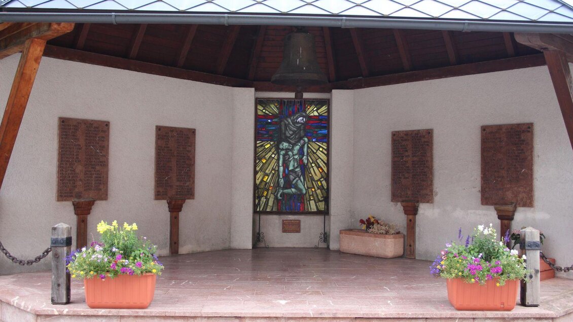 Eine Kapelle mit buntem Glasfenster und Blumenarrangements. An den Wänden sind Gedenktafeln angebracht. | © Viola Lechner