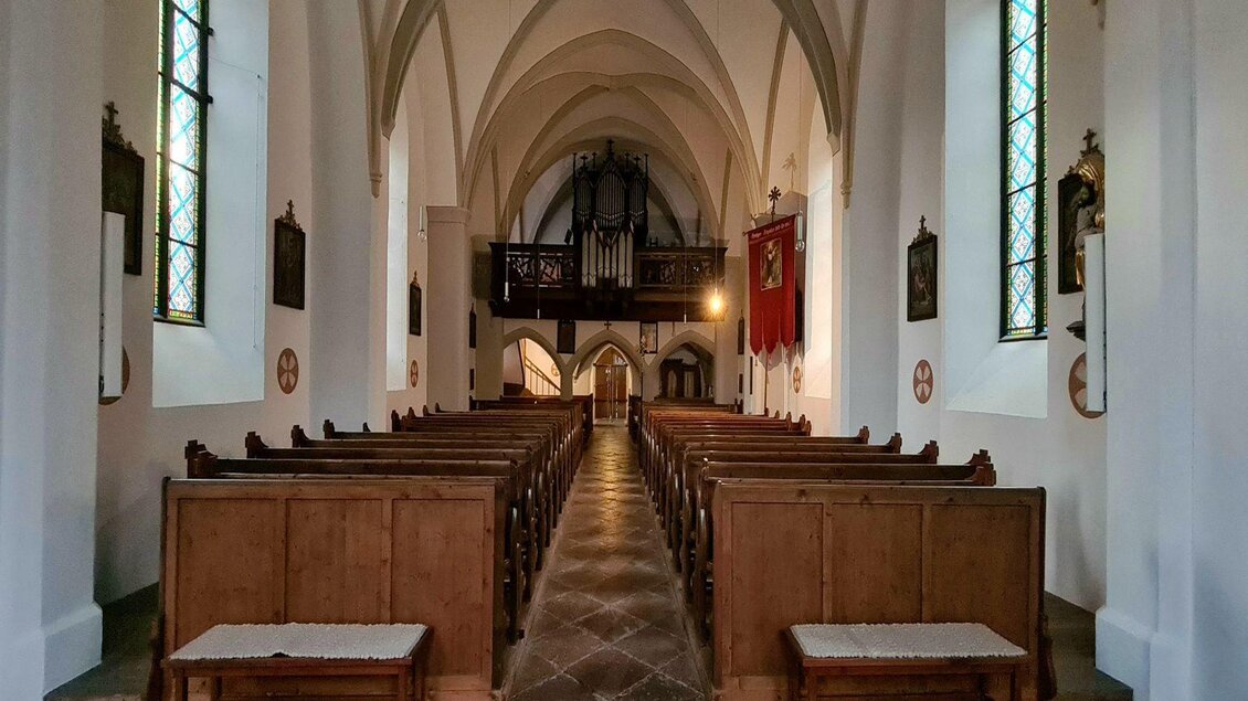 Eine ruhige Kirche mit Holzbankreihen und einem erhöhten Bereich für den Altar. Der Raum hat hohe Decken und große Fenster mit buntem Licht. | © Stephanie Bor