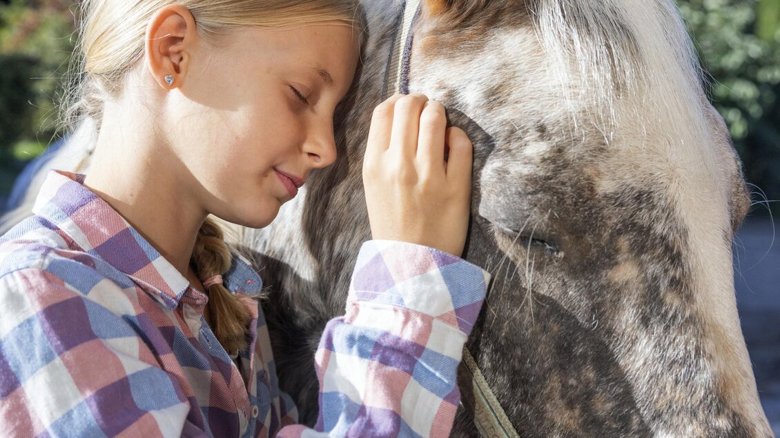 Ein Mädchen streichelt sanft ein Pferd und schließt dabei die Augen. Die Szene vermittelt eine liebevolle Verbindung zwischen dem Kind und dem Tier. | © www.zloam.at