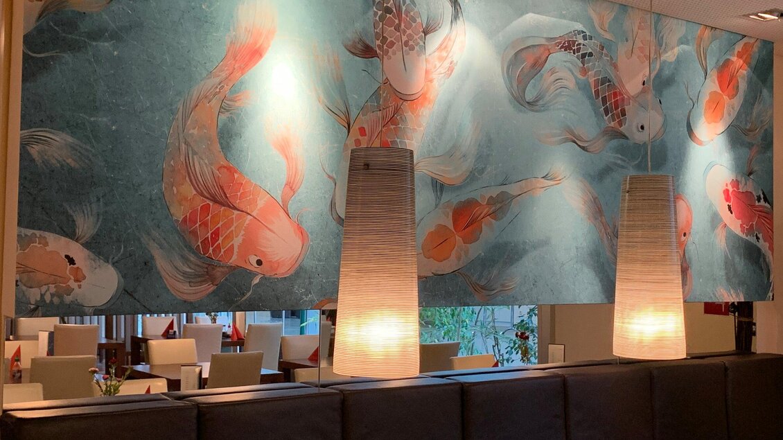 Ein stilvolles Restaurant mit einer Wandmalerei von Koi-Fischen. Zwei moderne Lampen sorgen für eine angenehme Beleuchtung. | © Pho You