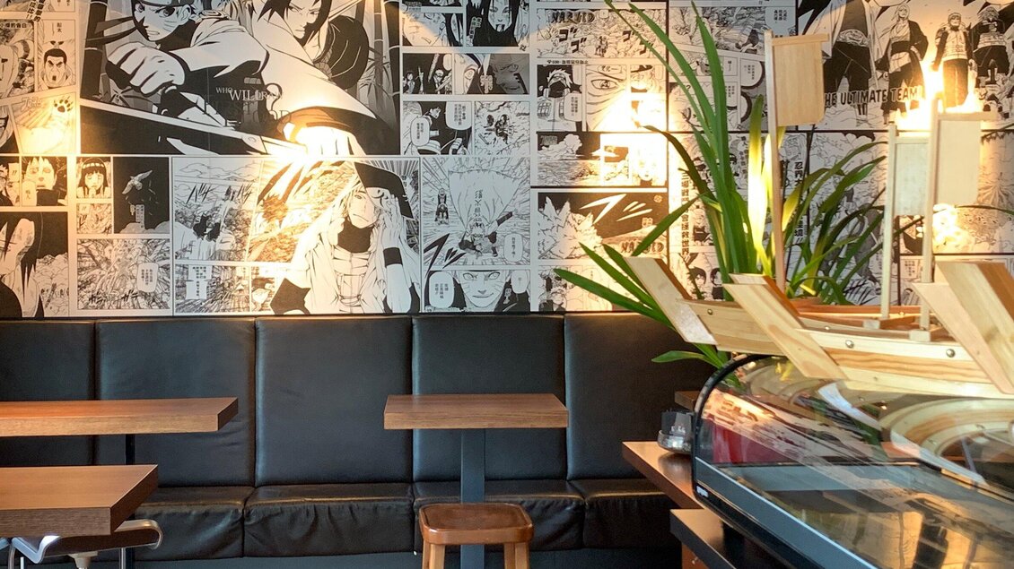 Ein modernes Café mit einer Wand voller Comics. Die Möbel sind schlicht und die Atmosphäre ist einladend. | © Pho You