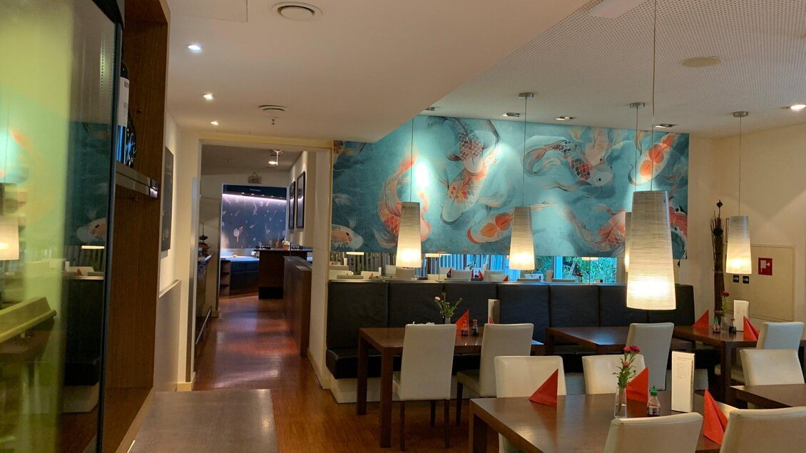 Ein modernes Restaurant mit Holzfußboden und eleganten Tischen. An der Wand befindet sich ein großes Gemälde mit bunten Fischen. | © Pho You