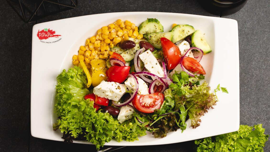 Ein bunter Salat mit frischem Gemüse, Feta-Käse und Mais. Die Zutaten sind schön angerichtet auf einem weißen Teller. | © Arvideo