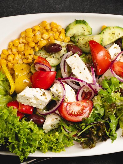 A colorful salad with fresh vegetables, feta cheese, and corn. The ingredients are beautifully arranged on a white plate. | © Arvideo