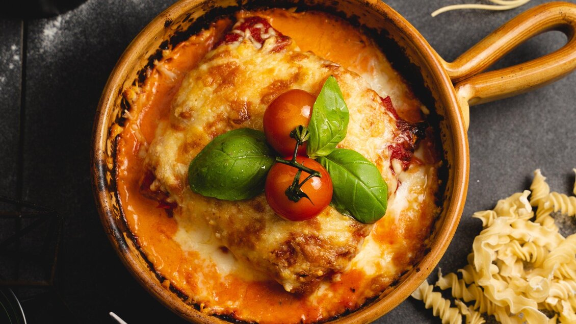 Ein köstliches Gericht in einer Tonpfanne, überbacken mit Käse und Tomaten. Frische Basilikumblätter verleihen dem Gericht eine besondere Note. | © Arvideo