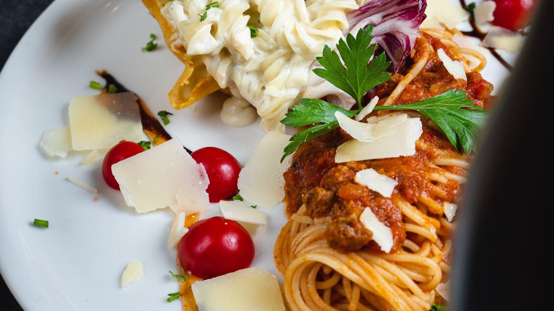 Ein Teller mit Spaghetti in Tomatensauce und einem gefüllten Tortilla. Frische Kirschtomaten, Parmesan und grüne Kräuter ergänzen das Gericht. | © Arvideo