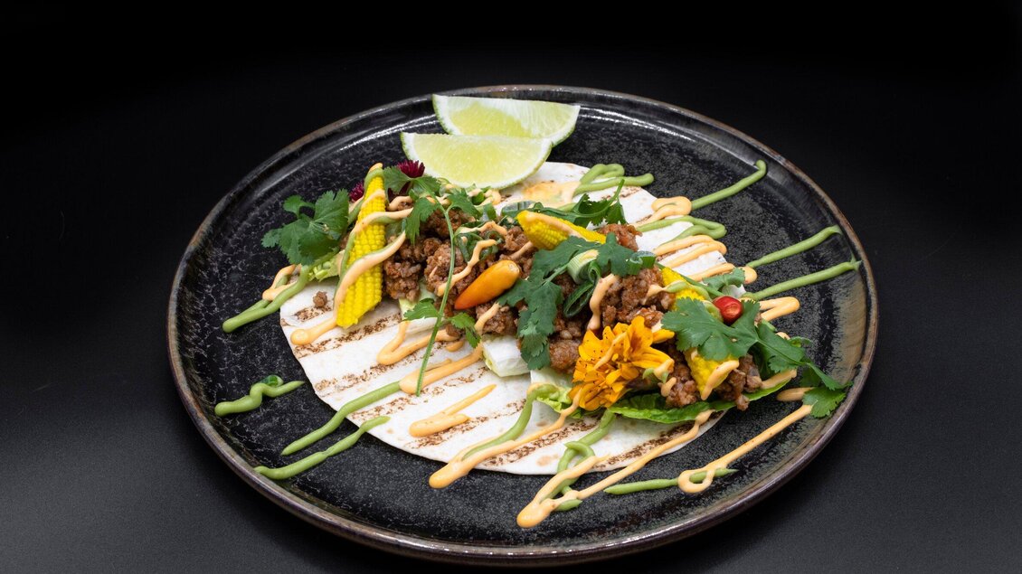 Ein kunstvoll angerichteter Teller mit Tacos, belegt mit frischem Gemüse und einer würzigen Sauce. Dazu liegen Limettenscheiben, die das Gericht ergänzen. | © Aiola - Jauk Katharina