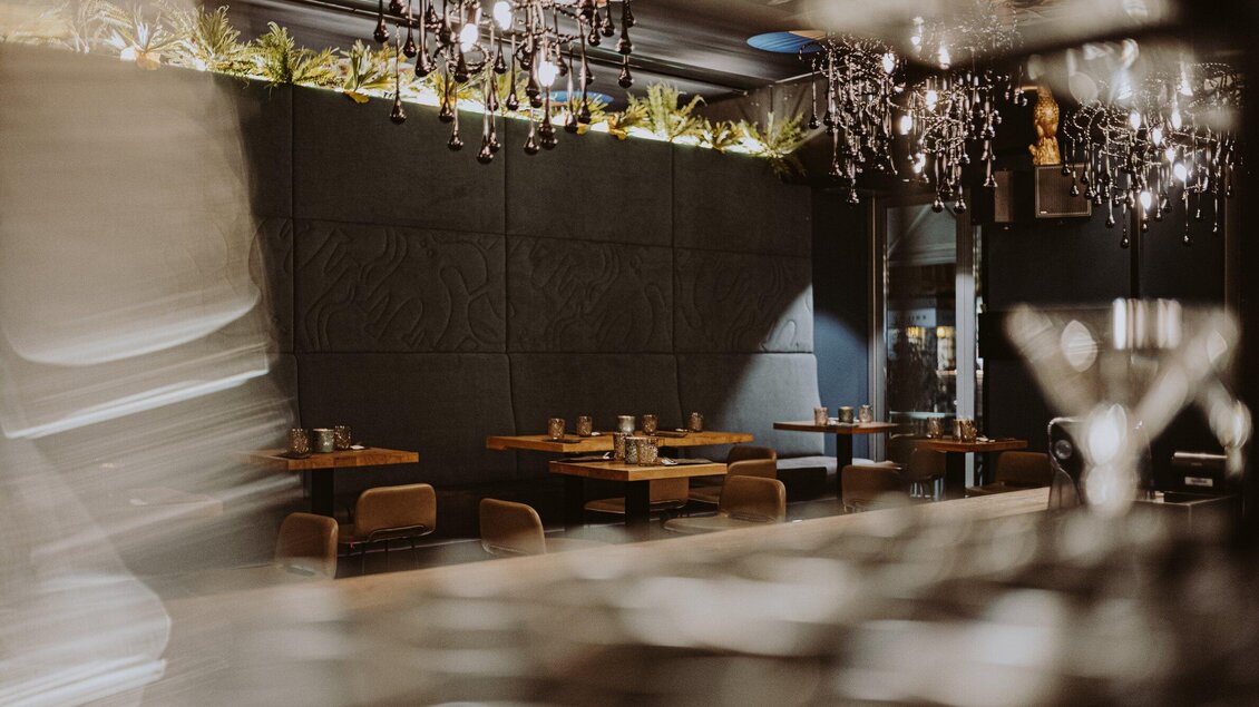 Ein modernes Restaurant mit stilvoller Einrichtung und eleganten Kronleuchtern. Die Tische sind ordentlich gedeckt und schaffen eine einladende Atmosphäre. | © Aiola - Joel Kernasenko