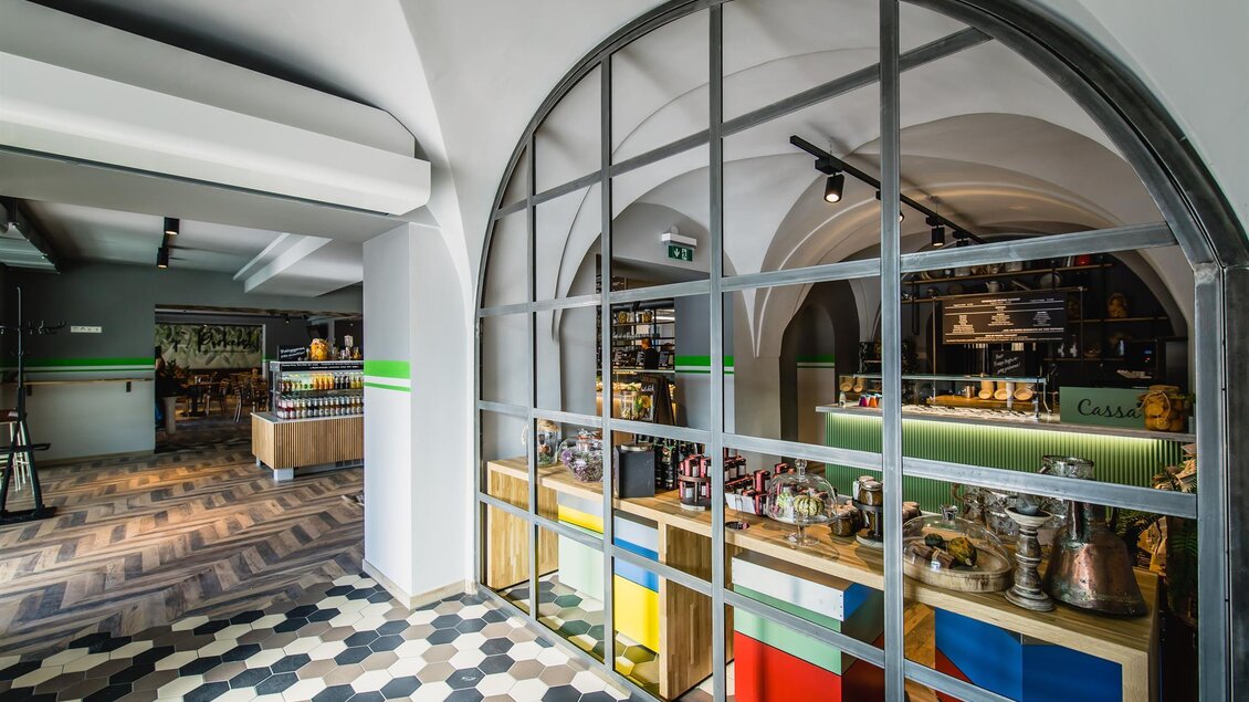 Ein modernes Café mit einem stilvollen Interieur und bunten Regalen. Die großen Fenster lassen viel Licht herein und schaffen eine einladende Atmosphäre. | © Pirker GmbH Mariazell