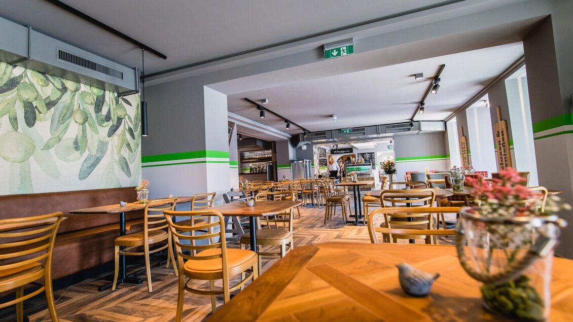 Ein modernes Restaurant mit Holzstühlen und Tischen. Die Wände sind hell und mit grünen Akzenten und Pflanzenbildern dekoriert. | © Pirker GmbH Mariazell
