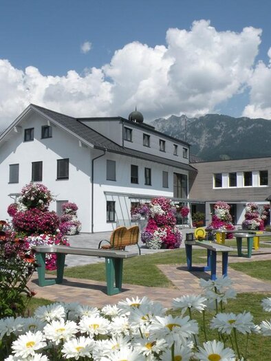 A beautiful garden with colorful flowers and modern benches. In the background, mountains and a bright blue sky can be seen. | © Marktgemeinde Haus