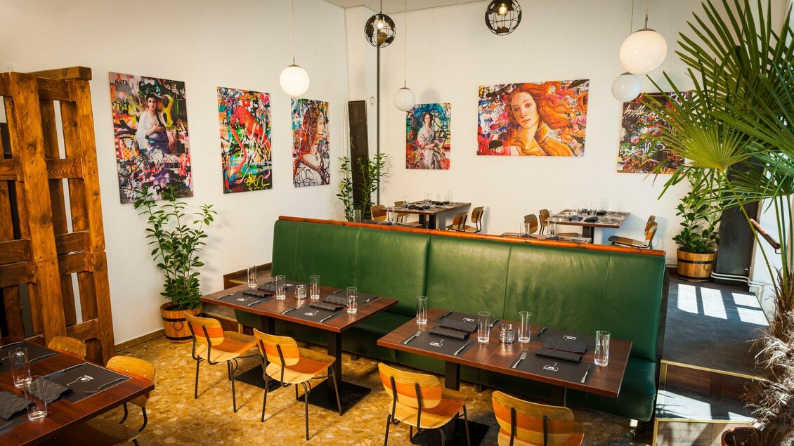 Ein modernes Restaurant mit einer einladenden Atmosphäre. Bunte Kunstwerke schmücken die Wände, und die Tische sind dekorativ gedeckt. | © Pizzaiolo