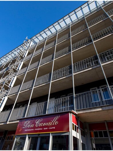 Ein modernes Gebäude mit einem Restaurant namens "Don Camillo" im Erdgeschoss. Die Fassade hat viele Balkone und einen klaren blauen Himmel im Hintergrund. | © TV Region Graz - Lunghammer