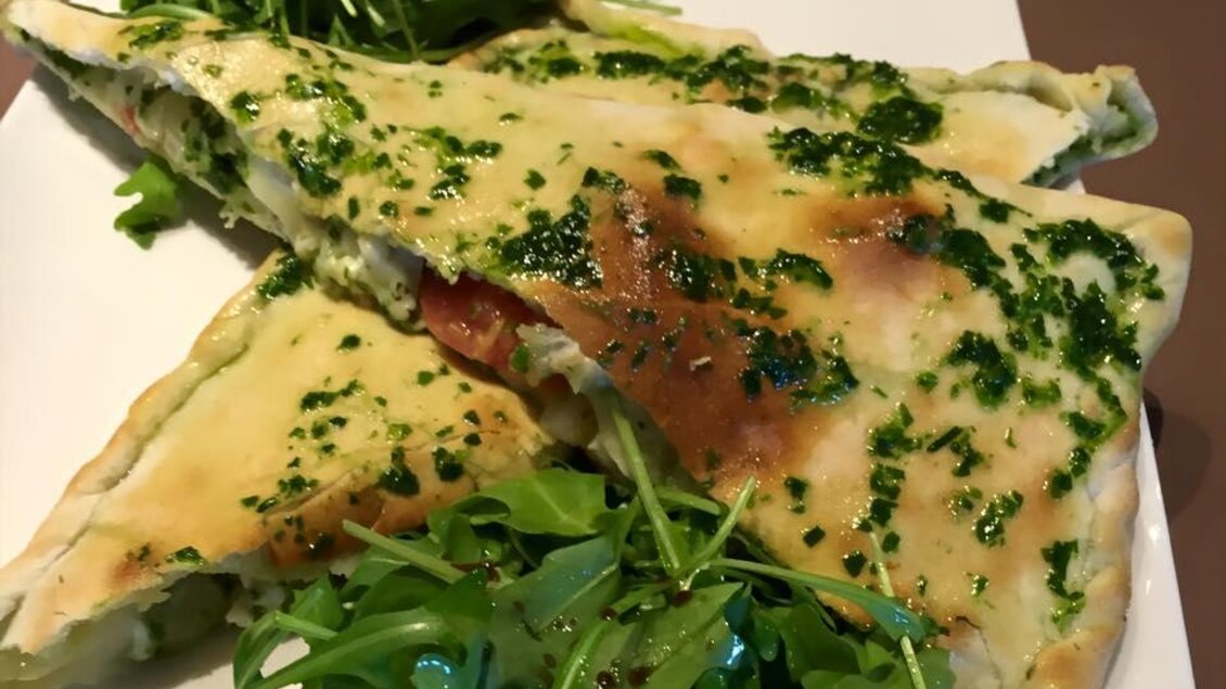 Ein Teller mit gefülltem Fladenbrot, garniert mit frischem Rucola und Kräutern. Das Brot hat eine goldene Farbe und einen köstlichen Belag. | © Pizzeria Fratelli