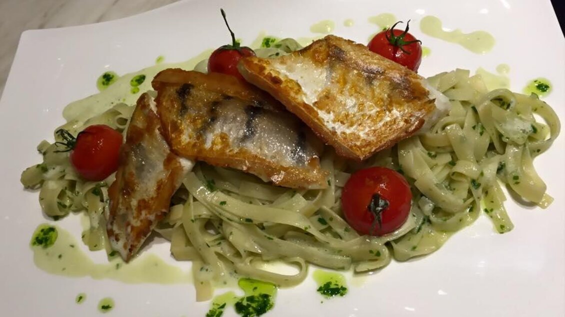 Ein Teller mit frisch zubereiteten Fettuccine und gebratenem Fisch. Dazu glänzende Kirschtomaten und ein grünes Pesto. | © Pizzeria Fratelli