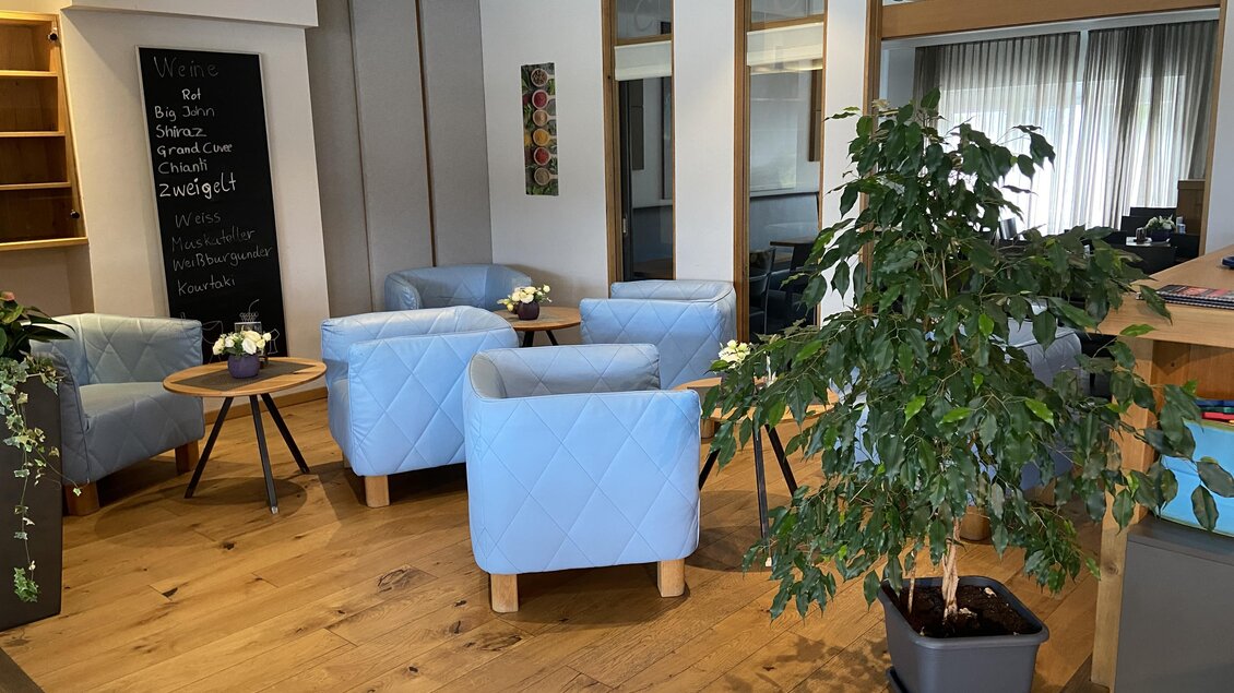 Ein gemütlicher Wartebereich mit blauen Sesseln und einem kleinen Tisch. Im Hintergrund befindet sich eine begrünte Ecke mit einer Pflanze. | © Mamarosa