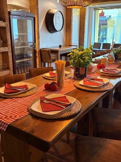 Ein stilvoll gedeckter Tisch in einem Restaurant mit Holzstühlen. Auf dem Tisch liegen bunte Servietten, Teller und frische Blumen. | © San Marco